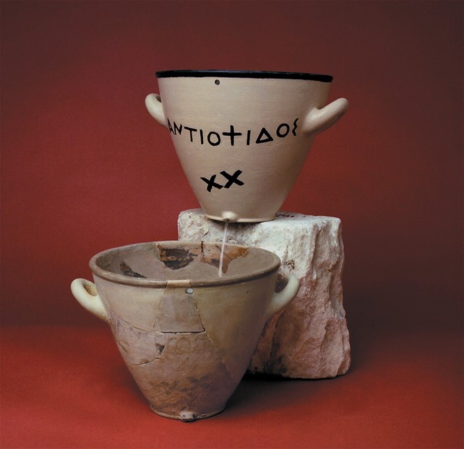 A Klepsydra (waterclock) used to time speeches in the Athenian courts. Original in front with replica above showing the flow of water out of the top pot into the lower one.